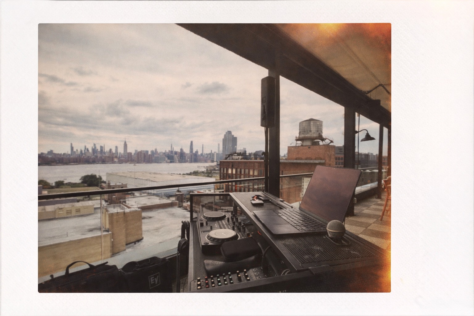 DJ setup with controller, laptop, and microphone overlooking the New York City skyline.