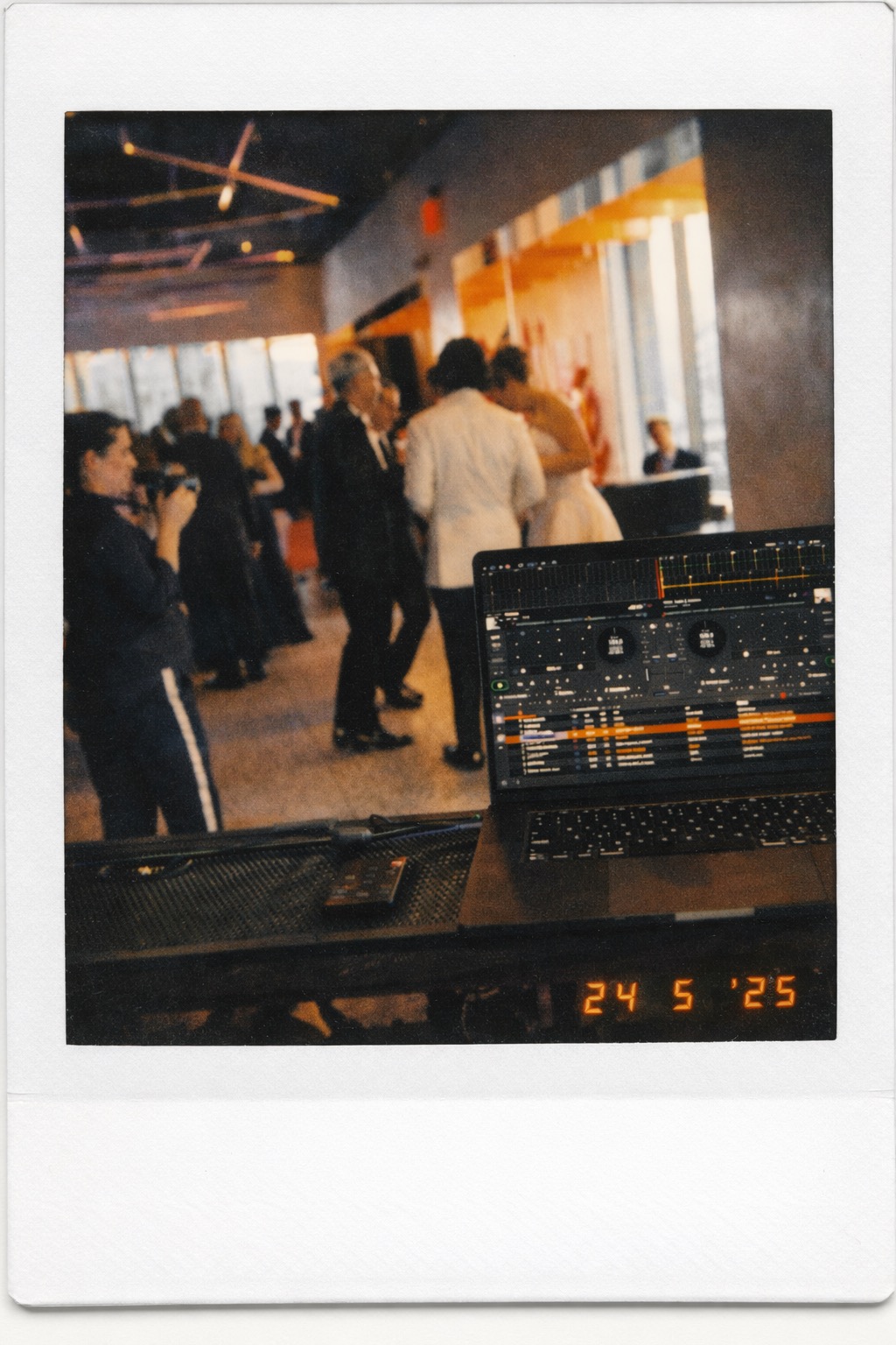 Polaroid photo of a dance floor from behind the DJ booth with a laptop and guests in motion.