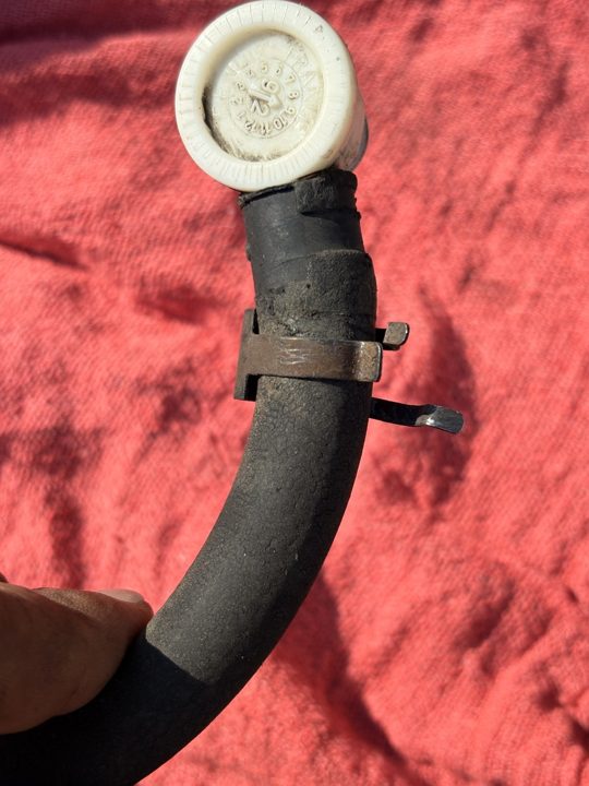 The old brake booster check valve on its hose: hard, cracked, held by a rusty spring clamp.